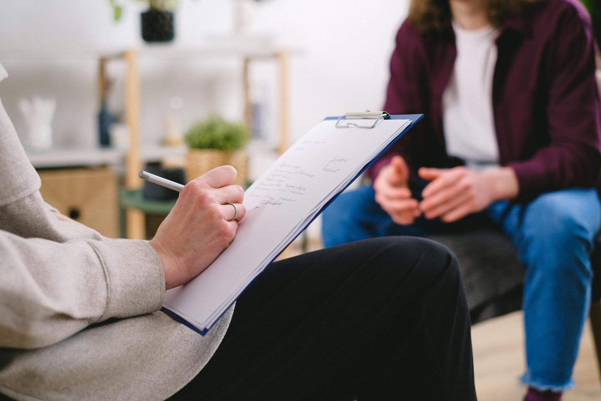 Close-up of a therapist writing notes on a clipboard while conversing with a patient.